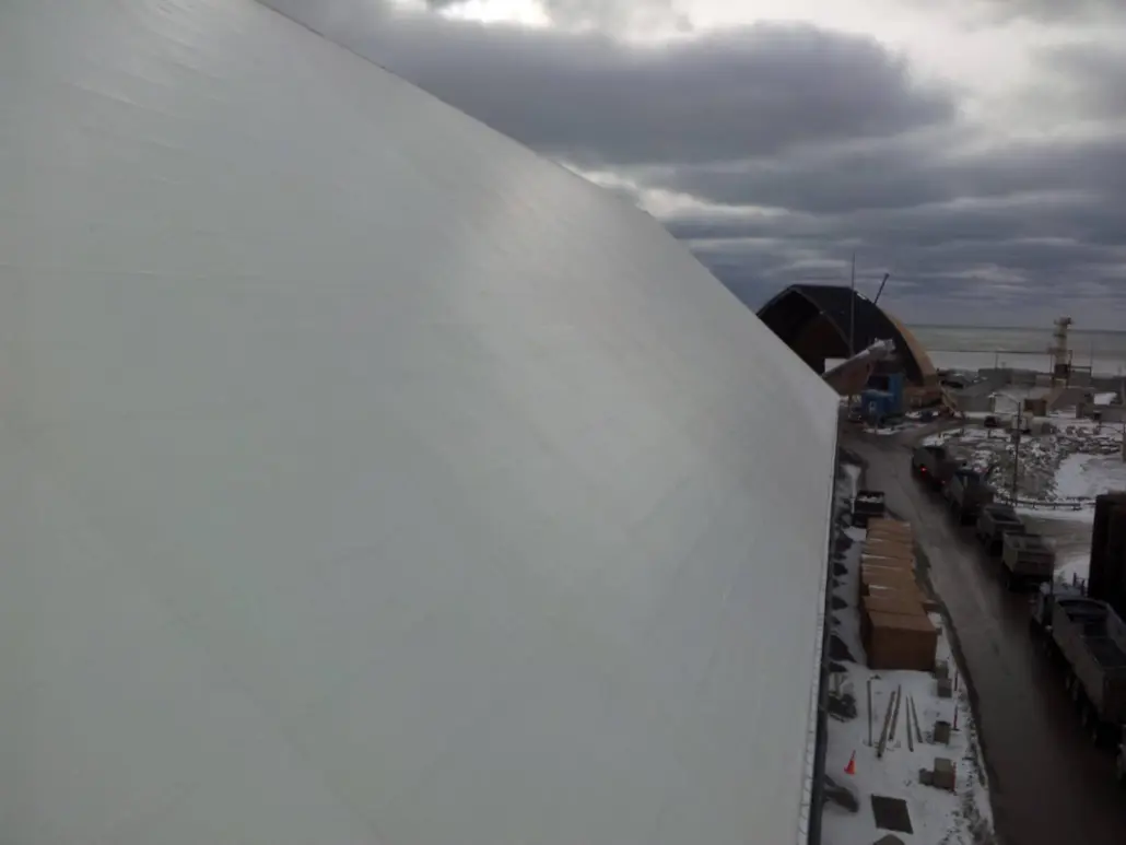 View along a curved white roof surface during winter work, with material staged on the ground below