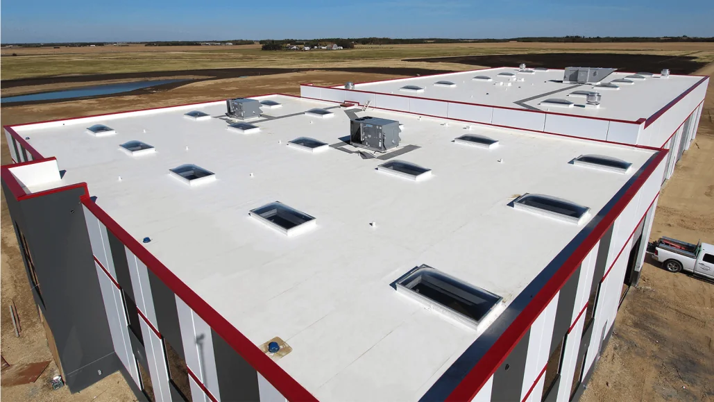 Aerial view of a newly completed industrial building with a white membrane roof, skylights and red edge trim