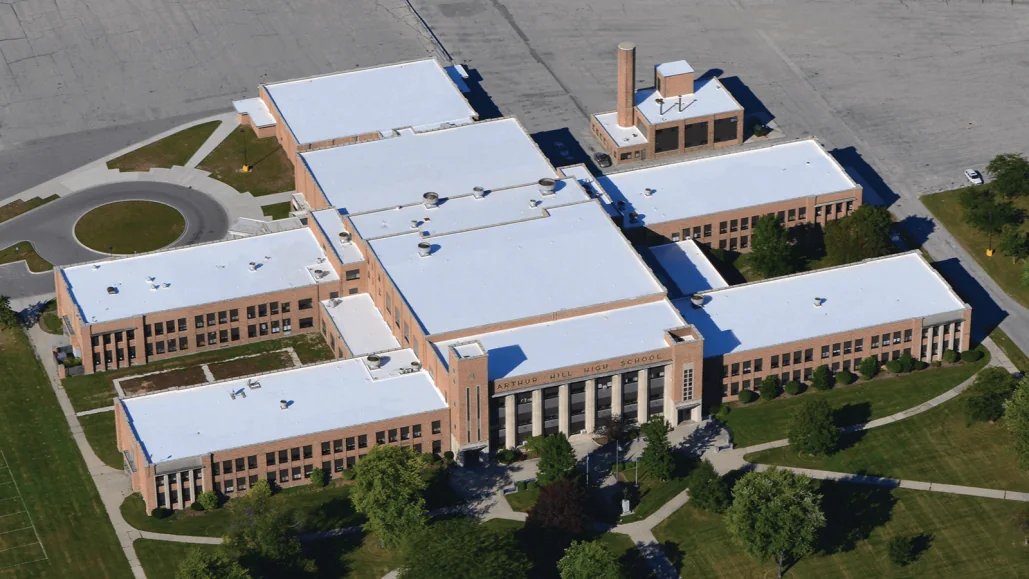 Aerial view of a large institutional building with white low-slope roof sections over a brick structure