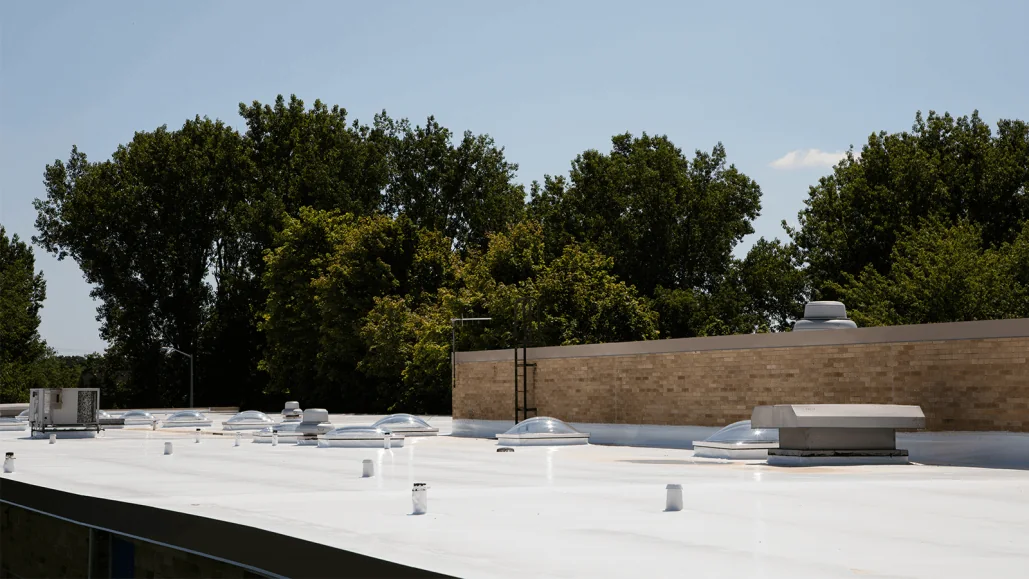 Roof-level view across a white membrane roof with skylights, vents and a masonry screen wall