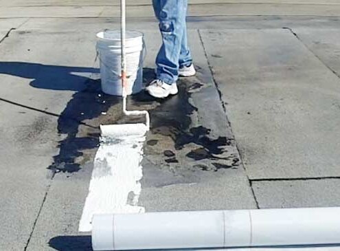 Roofing professional applying leveling compound to fix ponding water on a flat roof.