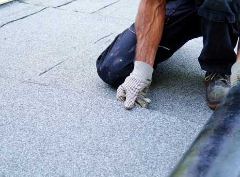 A roofing contractor installing roll roofing on a flat roof with precise nail placement.