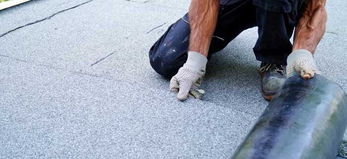 A roofing contractor installing roll roofing on a flat roof with precise nail placement.