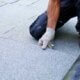 A roofing contractor installing roll roofing on a flat roof with precise nail placement.